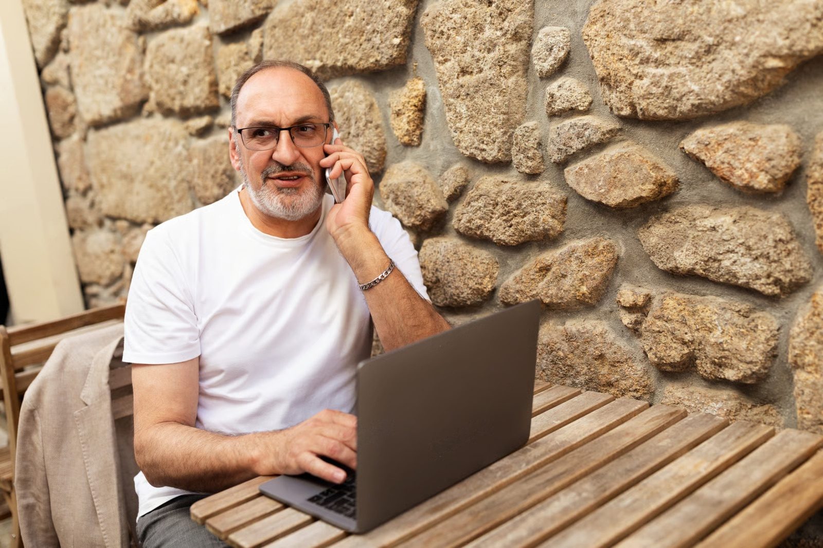 Un señor habla por teléfono mientras usa su computadora portátil
