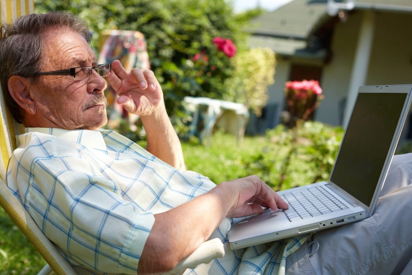 Un señor revisa su computadora portátil con atención en el patio de su casa