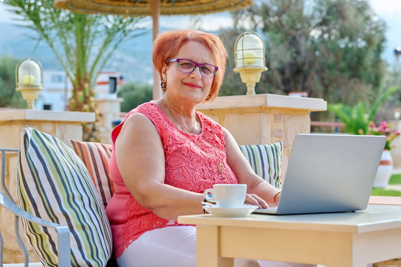 Una señora sonríe sentada frente a su computadora portátil en una terraza